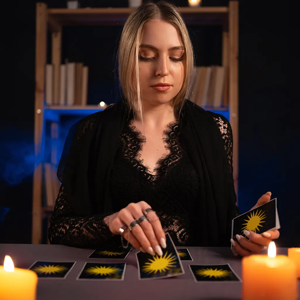 An image of a woman dealing tarot cards onto a table which has lit candles on